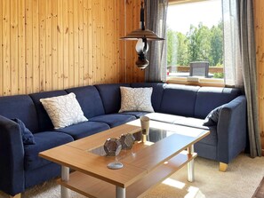 A cozy living room with a dark blue sofa, a glass coffee table, and a wooden ceiling.