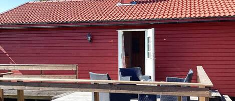 A red building with a chimney, a door, and a small outdoor seating area with chairs and a table.