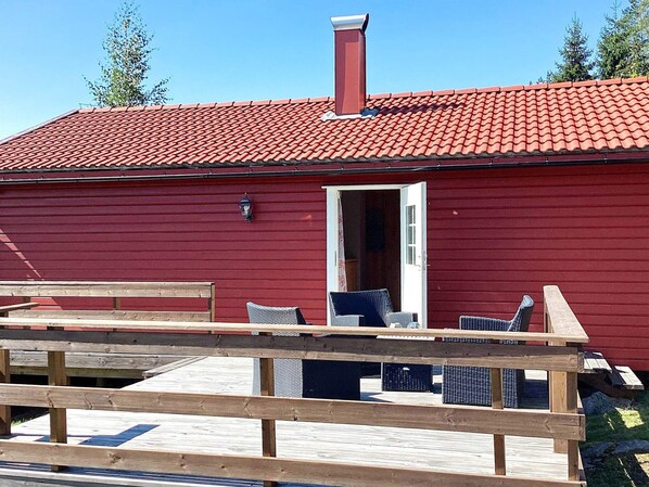 A red building with a chimney, a door, and a small outdoor seating area with chairs and a table.