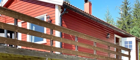 A red wooden house with a balcony, a chimney, and a window.