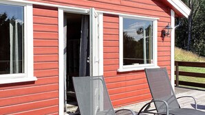 A red wooden building with two open sliding doors and a deck with two lounge chairs. - 4 Person Holiday Home in Bengtsfors (Bengtsfors)