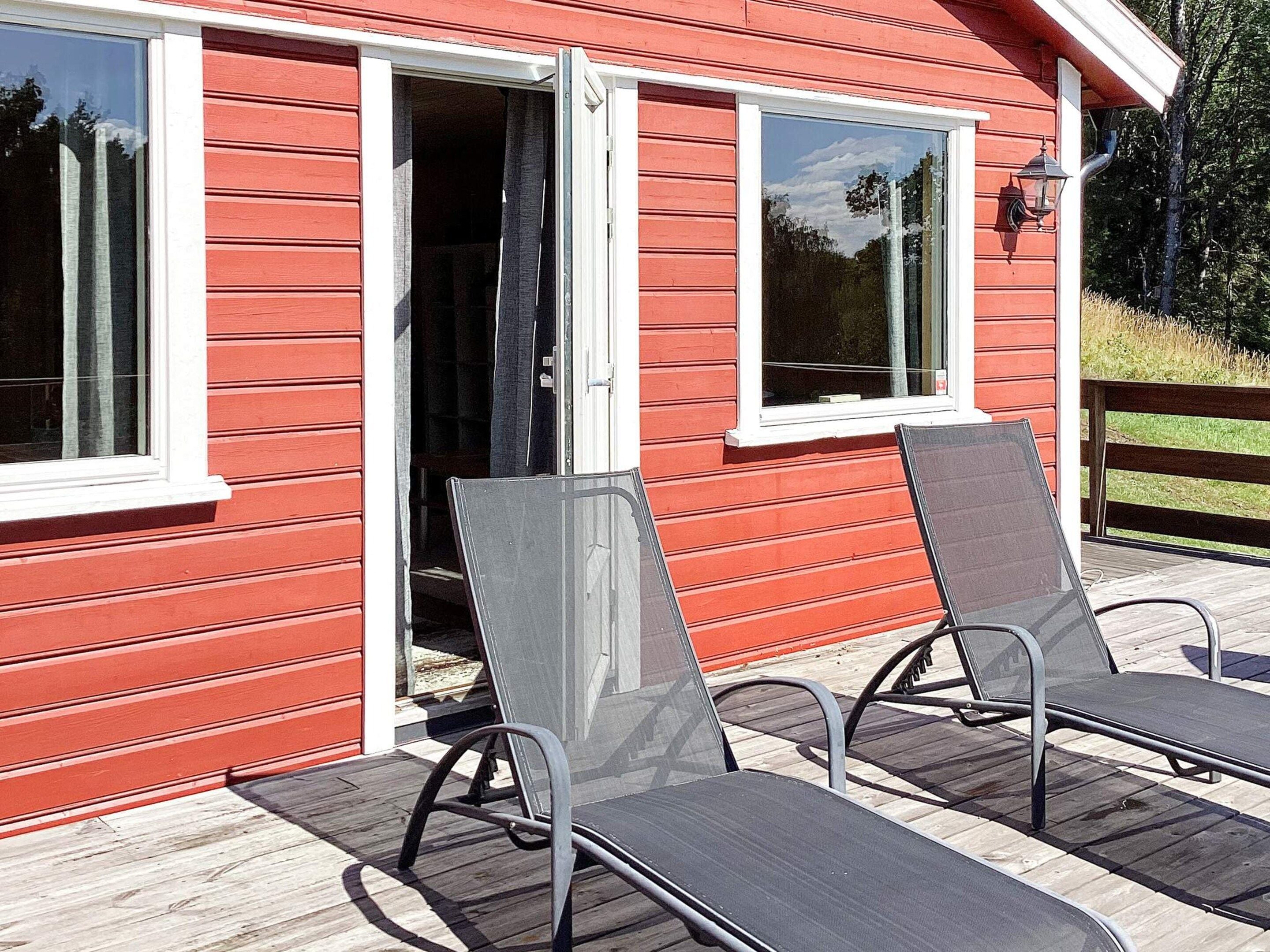 A red building with a sliding glass door, two outdoor chairs, and a wooden deck.