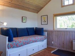 A room with a wooden ceiling, a white bench with blue cushions, a window with a view of trees, and two framed pictures on the wall. - 5 Person Holiday Home in Munkedal (Munkedal)