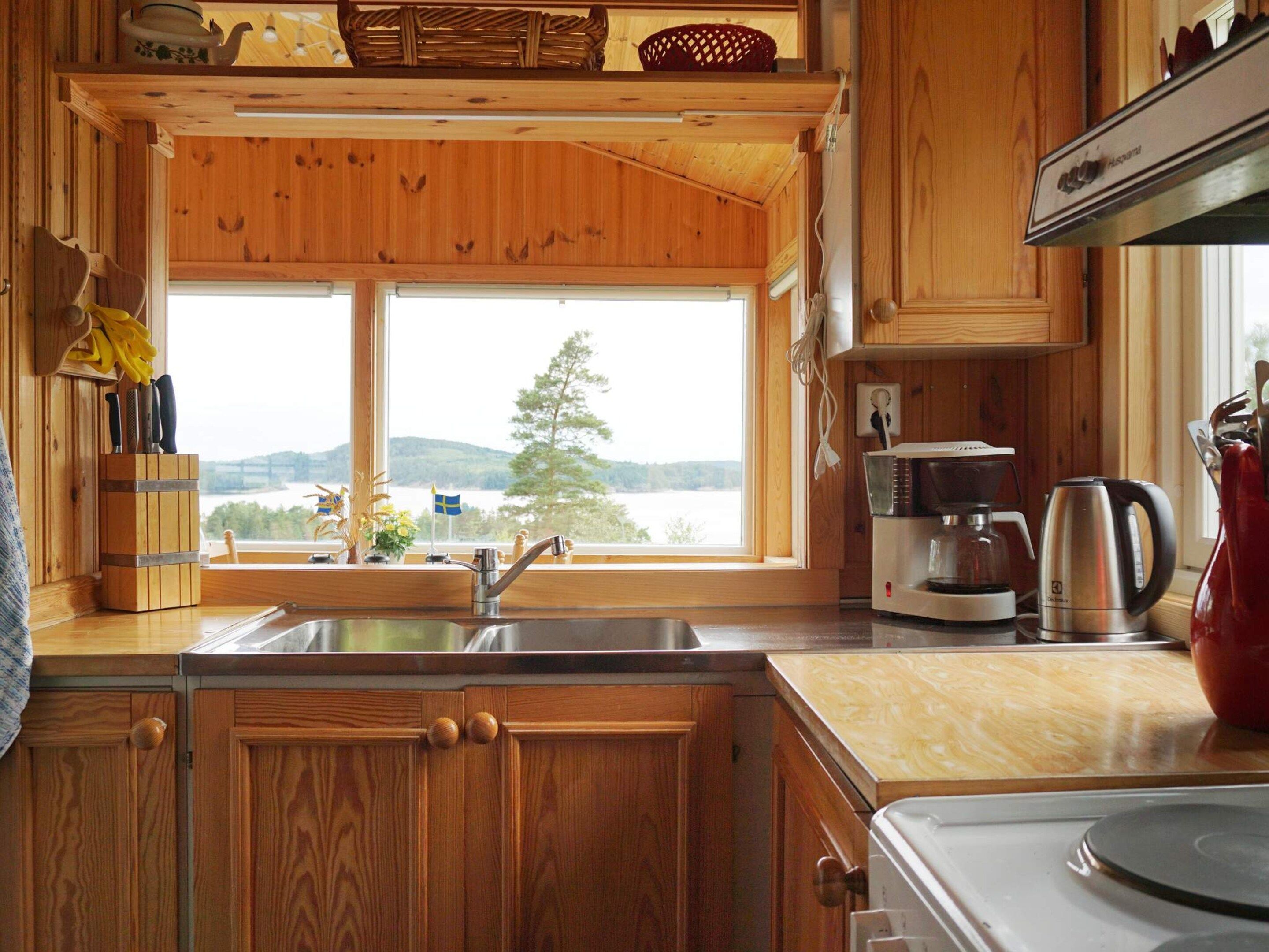 Cucina di una baita in legno con un'ampia finestra, mobili in legno ed elettrodomestici essenziali.