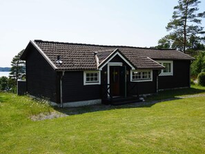 Ein zweistöckiges Holzhaus mit dunkler Fassade, einem Ziegeldach und einer kleinen Veranda.