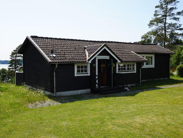 A single-story wooden house with a sloped roof, a front porch, and a small front yard.