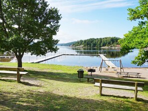 A lakeside park with a wooden bench, picnic table, and swing set. - 5 Person Holiday Home in Munkedal (Munkedal)