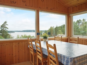A wooden cabin with a dining table and chairs, large windows with a view of a lake and forest. - 5 Person Holiday Home in Munkedal (Munkedal)