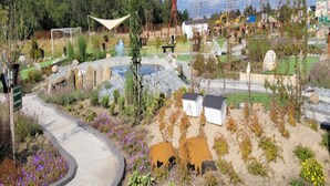 A garden with a winding path, a small pond, and a fenced area with cows.