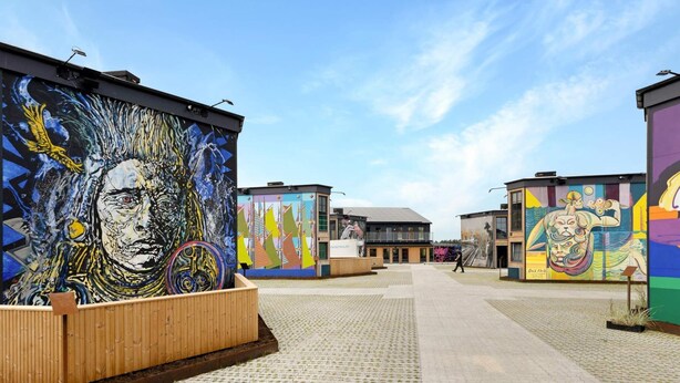 A modern building with vibrant murals on its exterior walls, a paved walkway, and a wooden bench area.