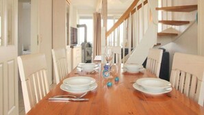 A dining room with a wooden table set for four, white chairs, and a staircase in the background. - Liebevoll Eingerichtetes Apartement (Rechlin)
