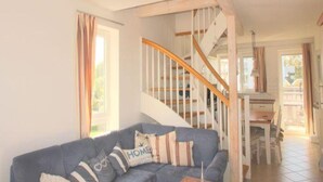 A living room with a blue sofa, a wooden staircase, and a dining area. - Liebevoll Eingerichtetes Apartement (Rechlin)