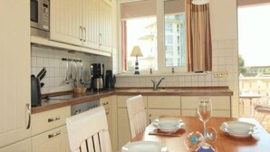 A modern kitchen with white cabinets, a built-in microwave, and a dining area with a wooden table set for two. - Liebevoll Eingerichtetes Apartement (Rechlin)