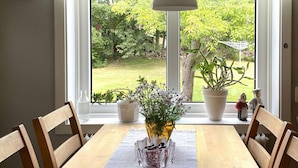 A dining table with chairs, a vase with flowers, and a view of a garden through a window. - 4 Star Holiday Home in Torso (Torsö)