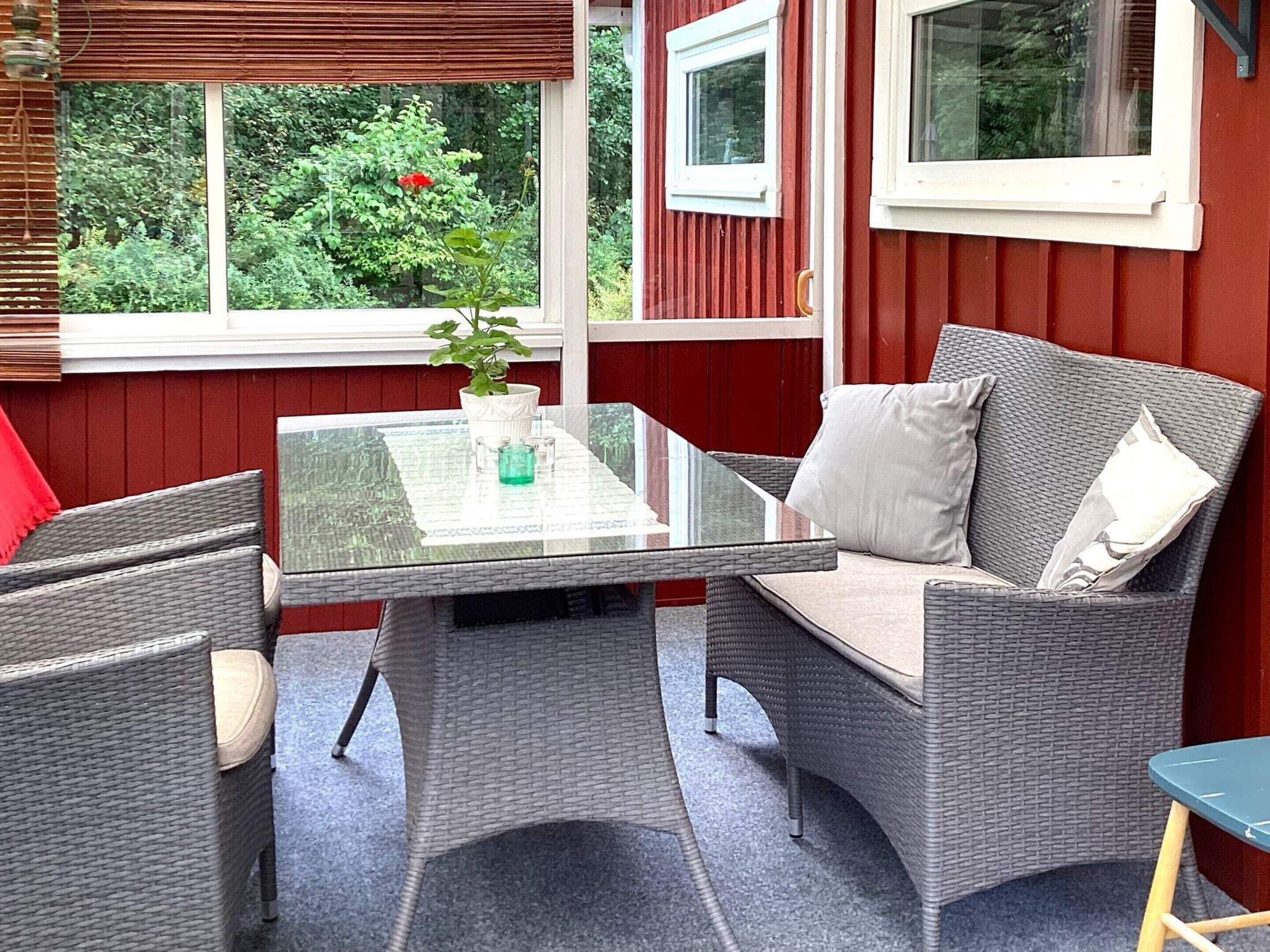 Una habitación con mesa de vidrio, muebles de mimbre y vistas al exterior con vegetación.