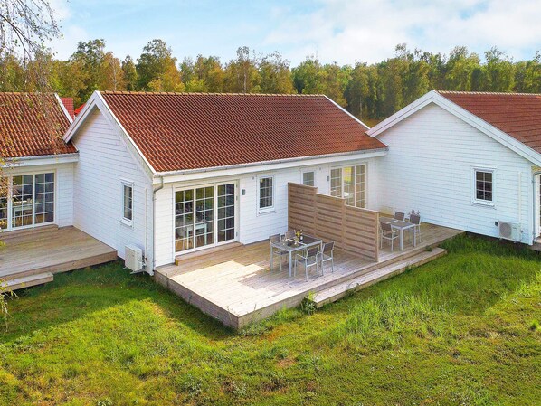A white building with a red roof, large windows, and a wooden deck with outdoor furniture.