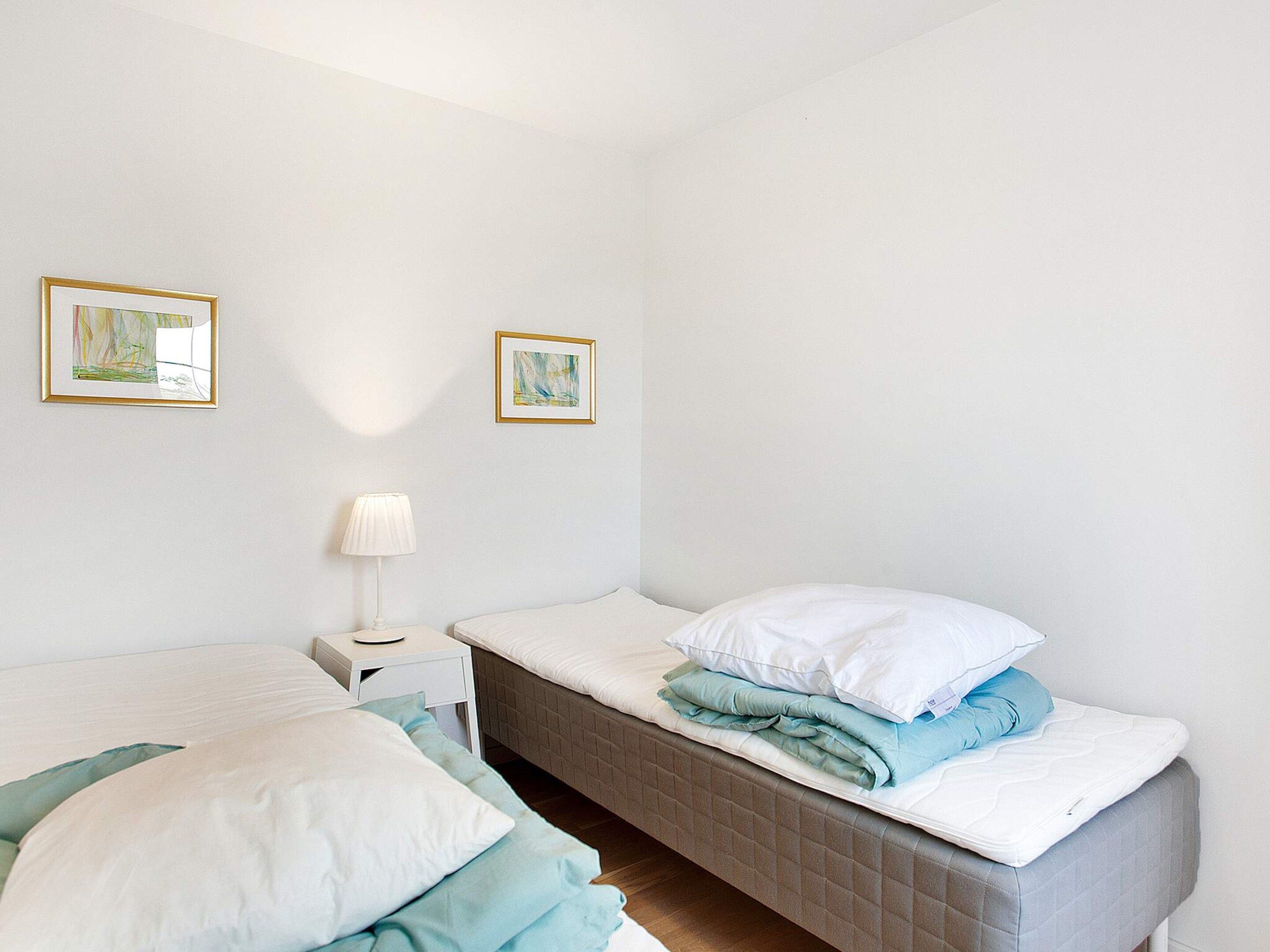 A bedroom with a bed, bedside table, lamp, and two framed pictures on the wall.
