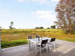 An outdoor dining area with a table and chairs on a wooden deck, overlooking a grassy field and trees. - 4 Person Holiday Park Home in Laeso (Læsø)