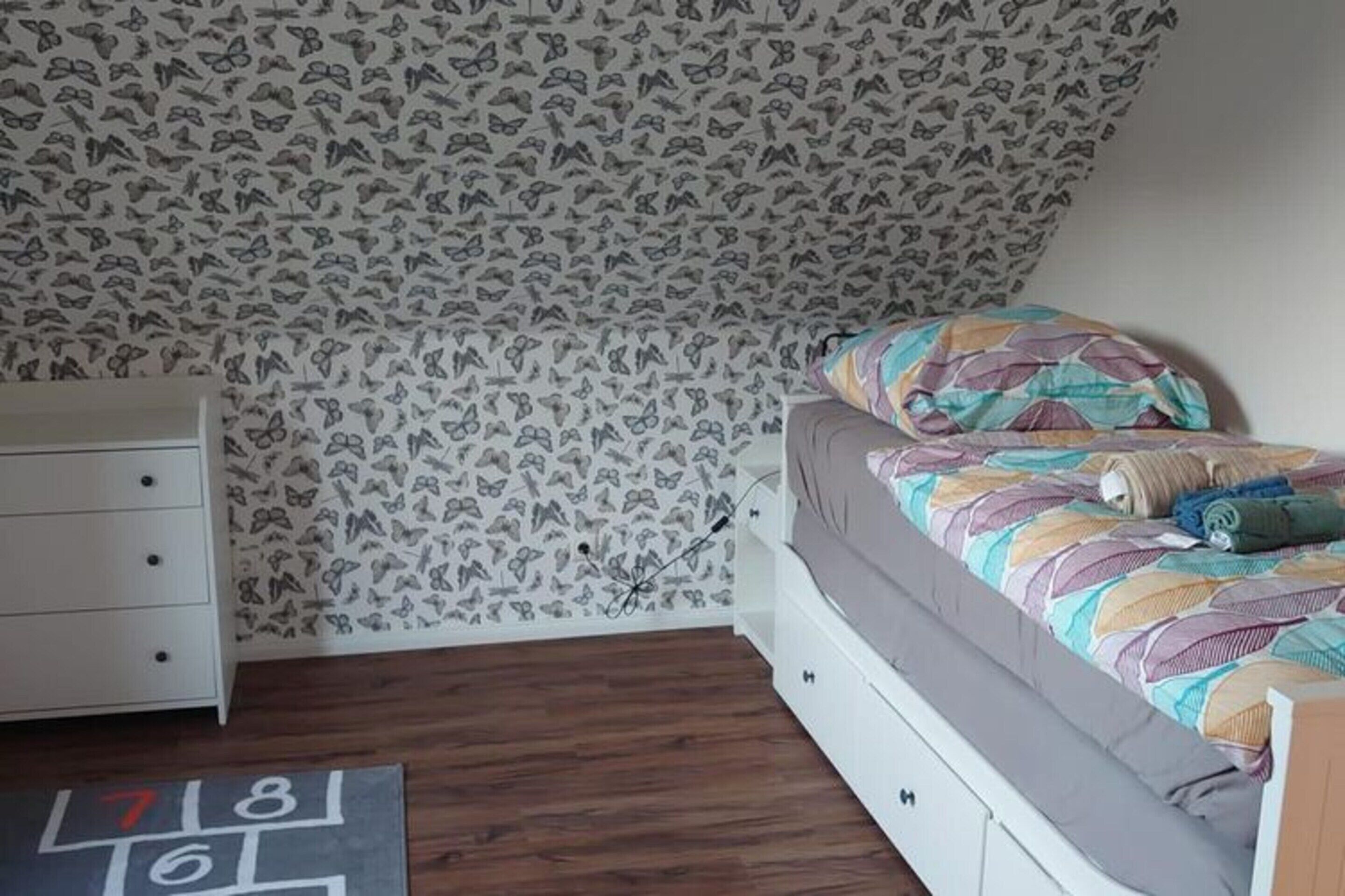 A bedroom with a bed, a dresser, and a patterned wallpaper.