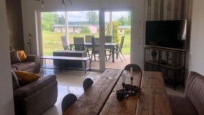 A living room with a wooden table, a sofa, a television, and a view of the outdoors. - Ferienhaus Seeluft in Klein Labenz (Warin)