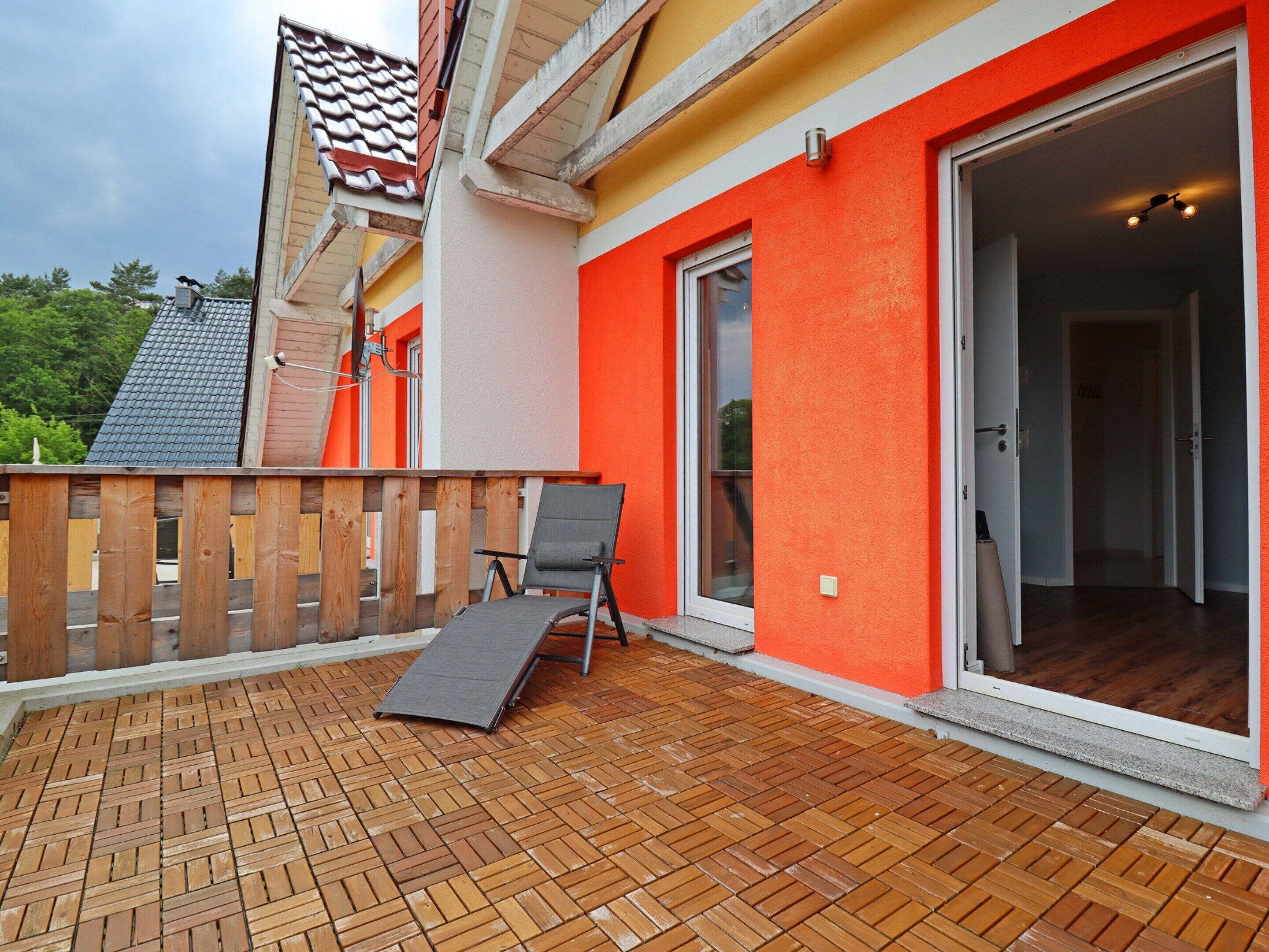 A covered patio with a wooden deck, a sliding glass door leading to an interior room, and a chair.
