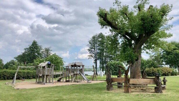A playground with a slide and climbing structures, surrounded by grass and trees. - Ferienhaus Seeluft in Klein Labenz (Warin)