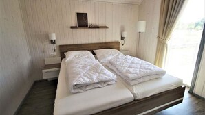 Ein Schlafzimmer mit einem hölzernen Kopfende, einem Nachttisch mit Lampe und einem Fenster mit Vorhängen.