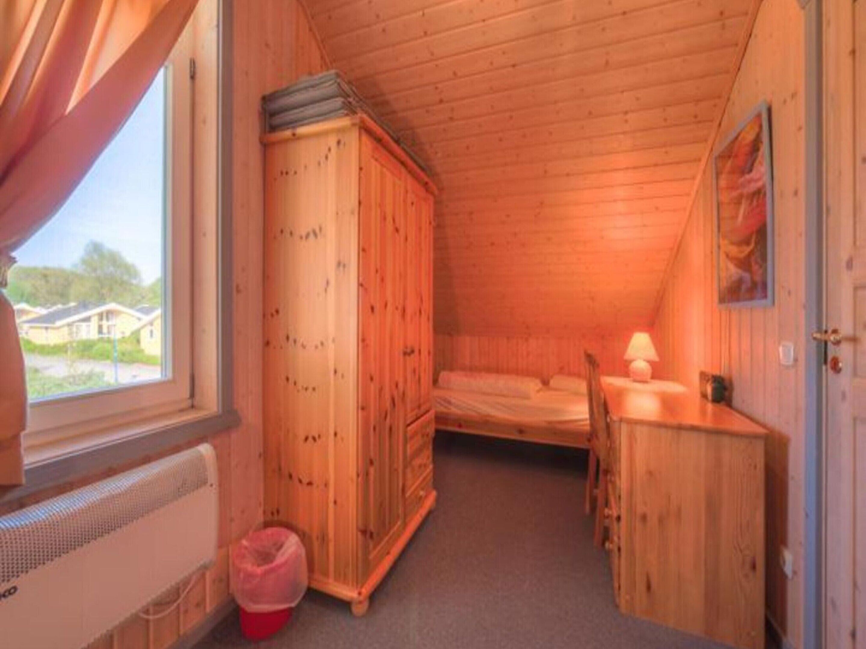 A small, wooden cabin room with a bed, a desk, and a wardrobe.