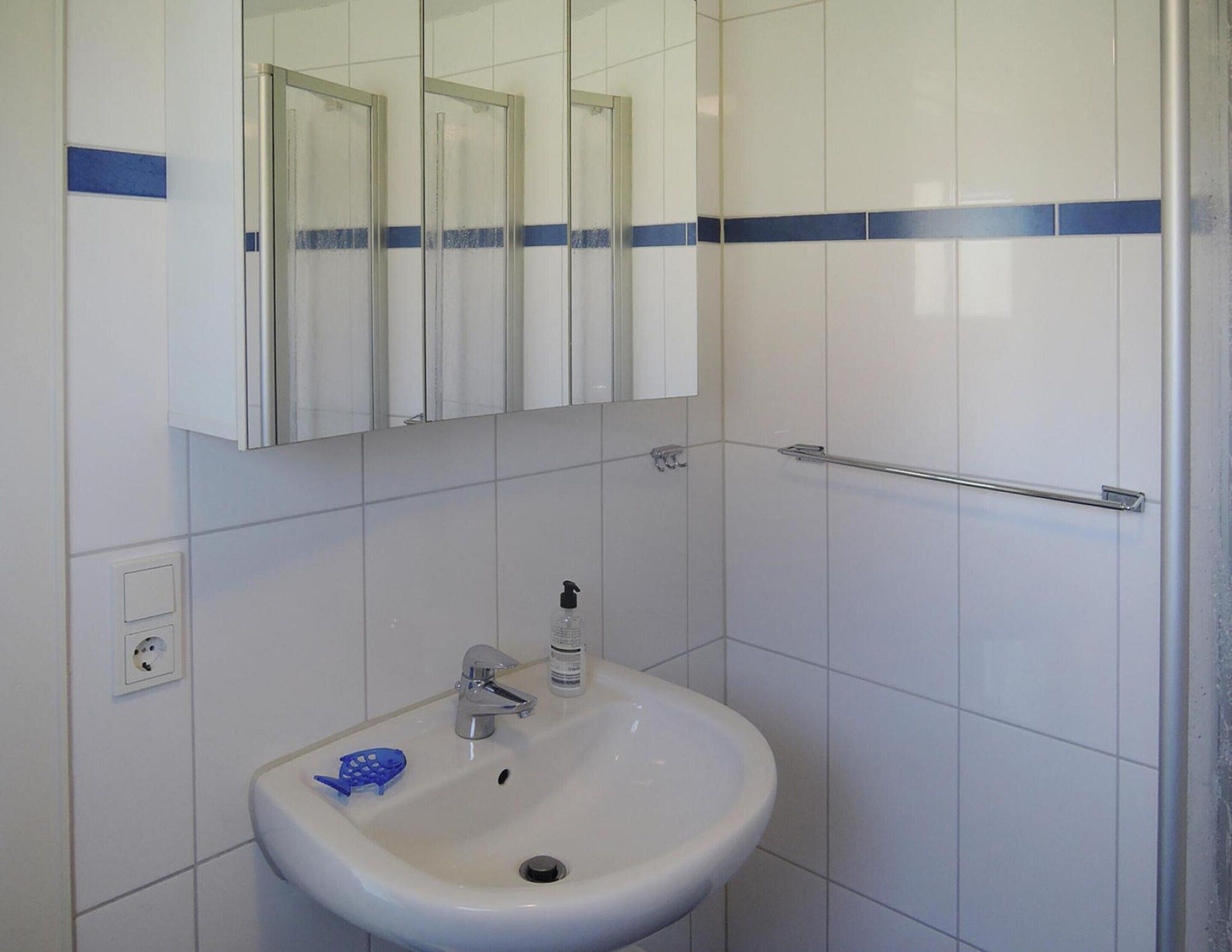 Une salle de bain avec un lavabo blanc, un miroir au-dessus et un porte-serviettes fixé au mur.