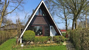 A modern, triangular-shaped house with a large glass window, surrounded by well-maintained gardens and trees. - Holiday Home in Burhave Near the sea (Butjadingen)