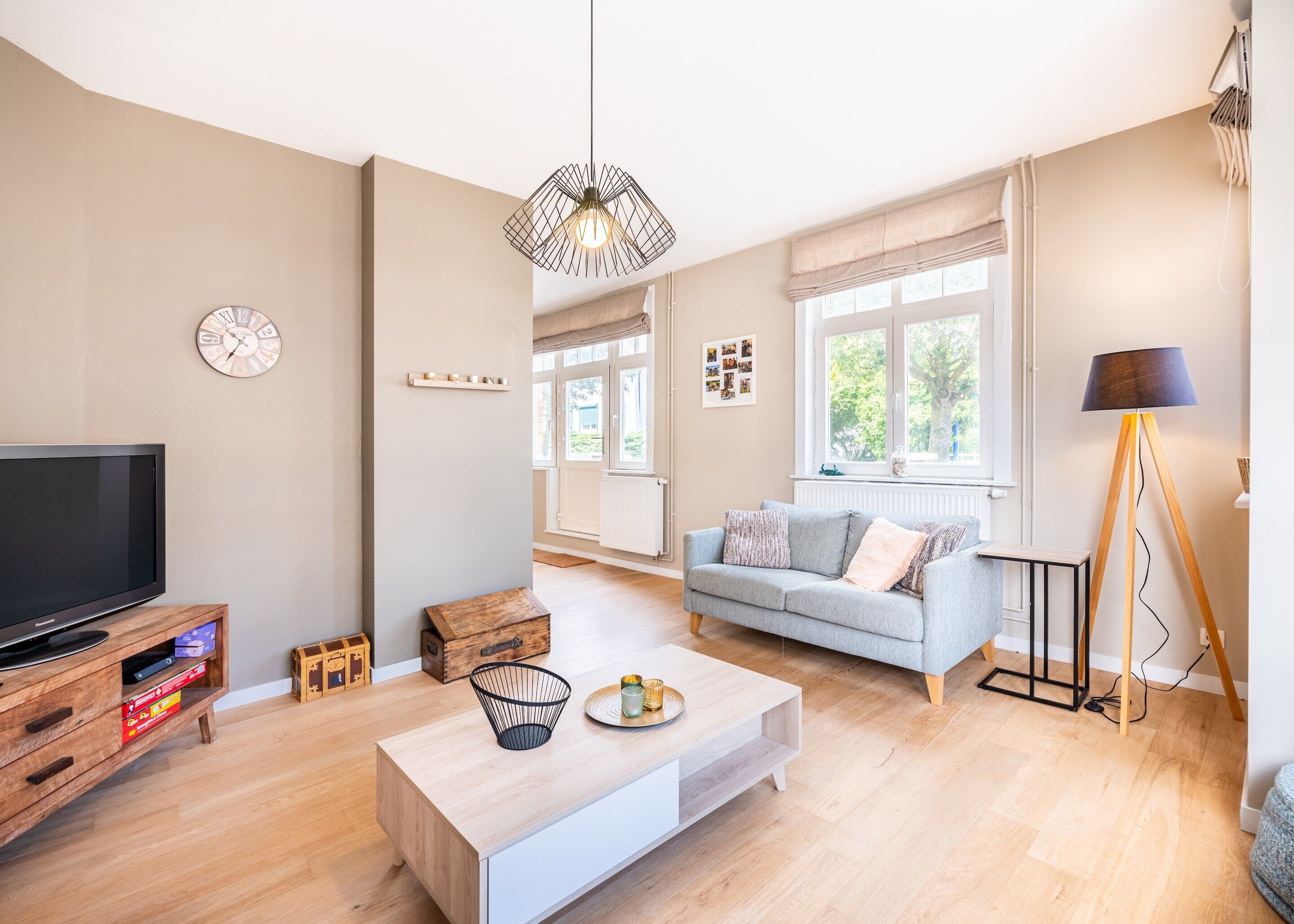 A modern living room with a flat-screen TV, a grey sofa, a wooden coffee table, and a floor lamp.
