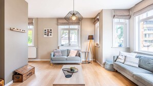 Een moderne woonkamer met een grijze bank, een houten salontafel en een vloerlamp.