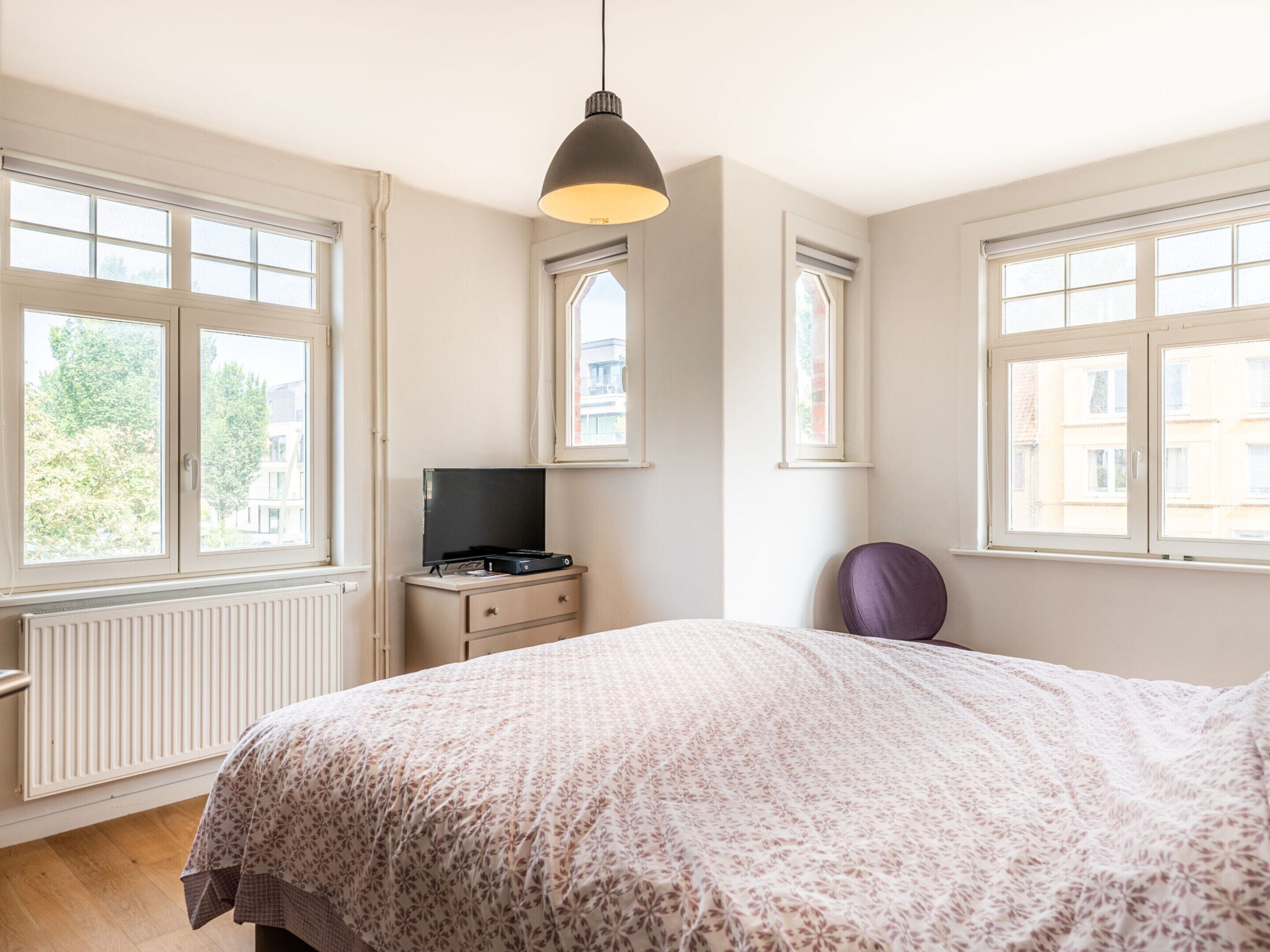 A bedroom with a bed, a dresser, a television, and a window.