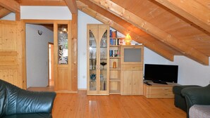 A cozy attic room with wooden beams, a TV, and a bookshelf. - Ferienhaus aus Holz in der Nahe des Skigebiets (Bayerisch Eisenstein)