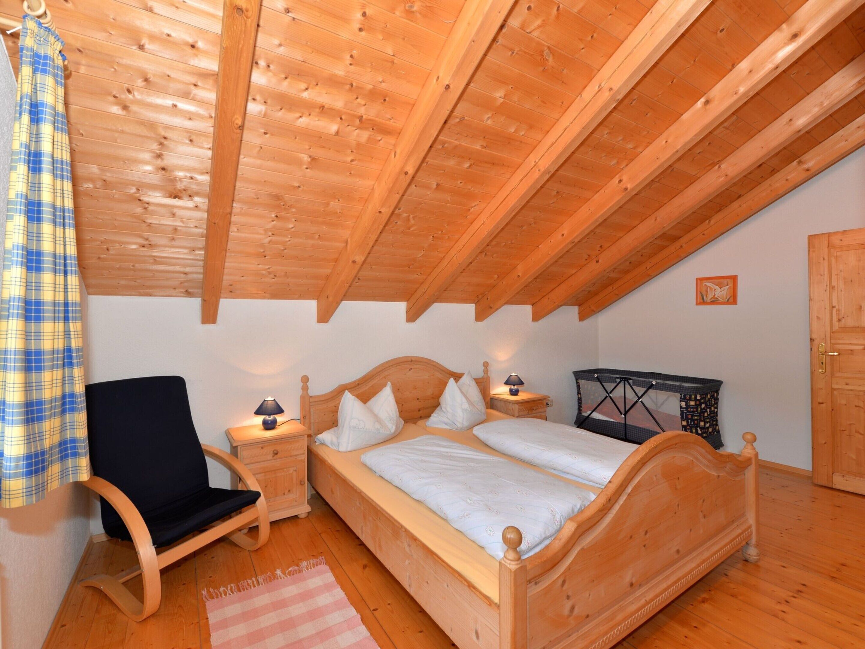 Ein gemütliches Schlafzimmer mit einem hölzernen Bett, einem Sessel, einem Nachttisch und einem kleinen Tisch.