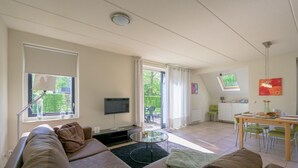 Ett rymligt vardagsrum med en stor soffa, en platt-TV och ett matbord med stolar.