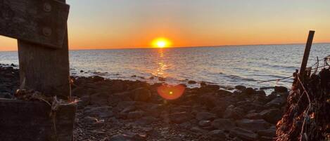 A sunset over a rocky beach with a wooden structure in the foreground.