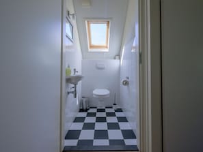 Une petite salle de bain avec un carrelage à motifs, une fenêtre, un lavabo et des toilettes.