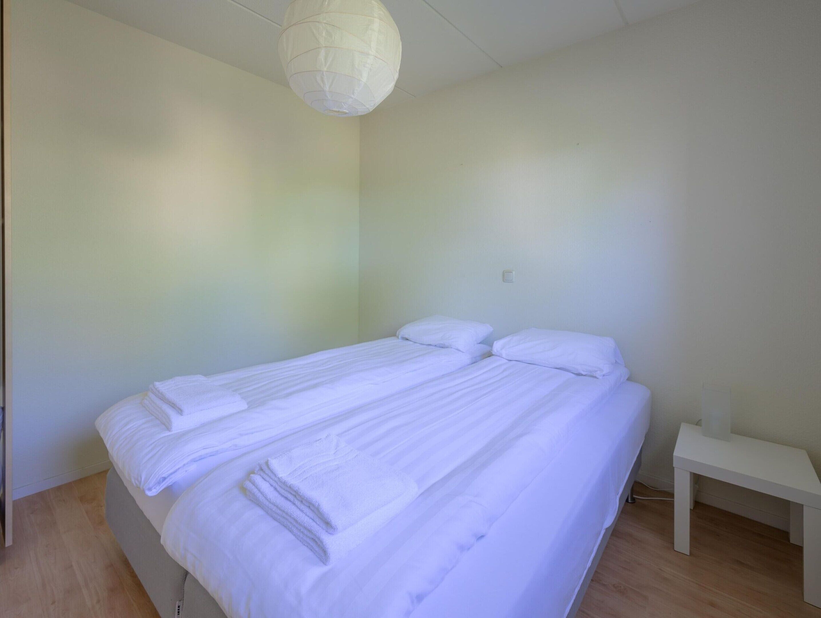 Ein schlichtes, minimalistisches Schlafzimmer mit einem Einzelbett, einem Nachttisch und einer Pendelleuchte.