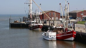 A harbor with several fishing boats docked, a red brick building, and a clear sky. - Reihenhaus, Dornumersiel (Dornum)