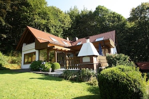 A two-story house with a sloped roof, wooden deck, and a small garden area. - Ferienwohnung Haus am Berg, Lonau (Herzberg am Harz)