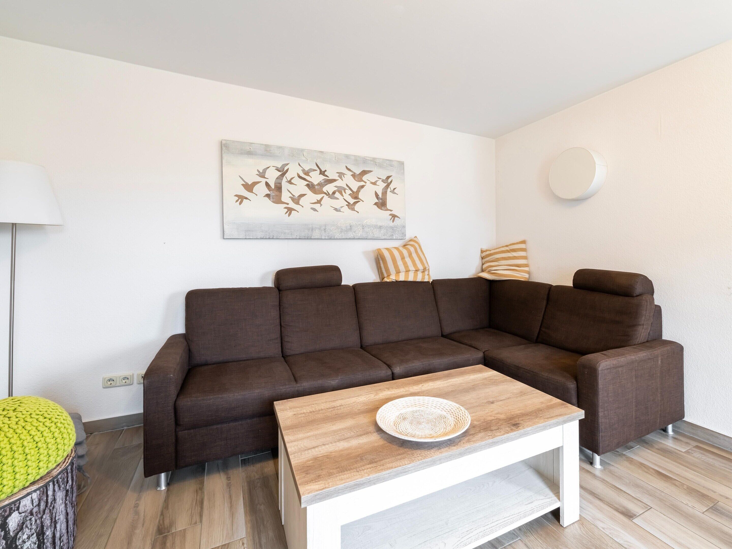 A modern living room with a brown sectional sofa, a wooden coffee table, and a wall-mounted light fixture.