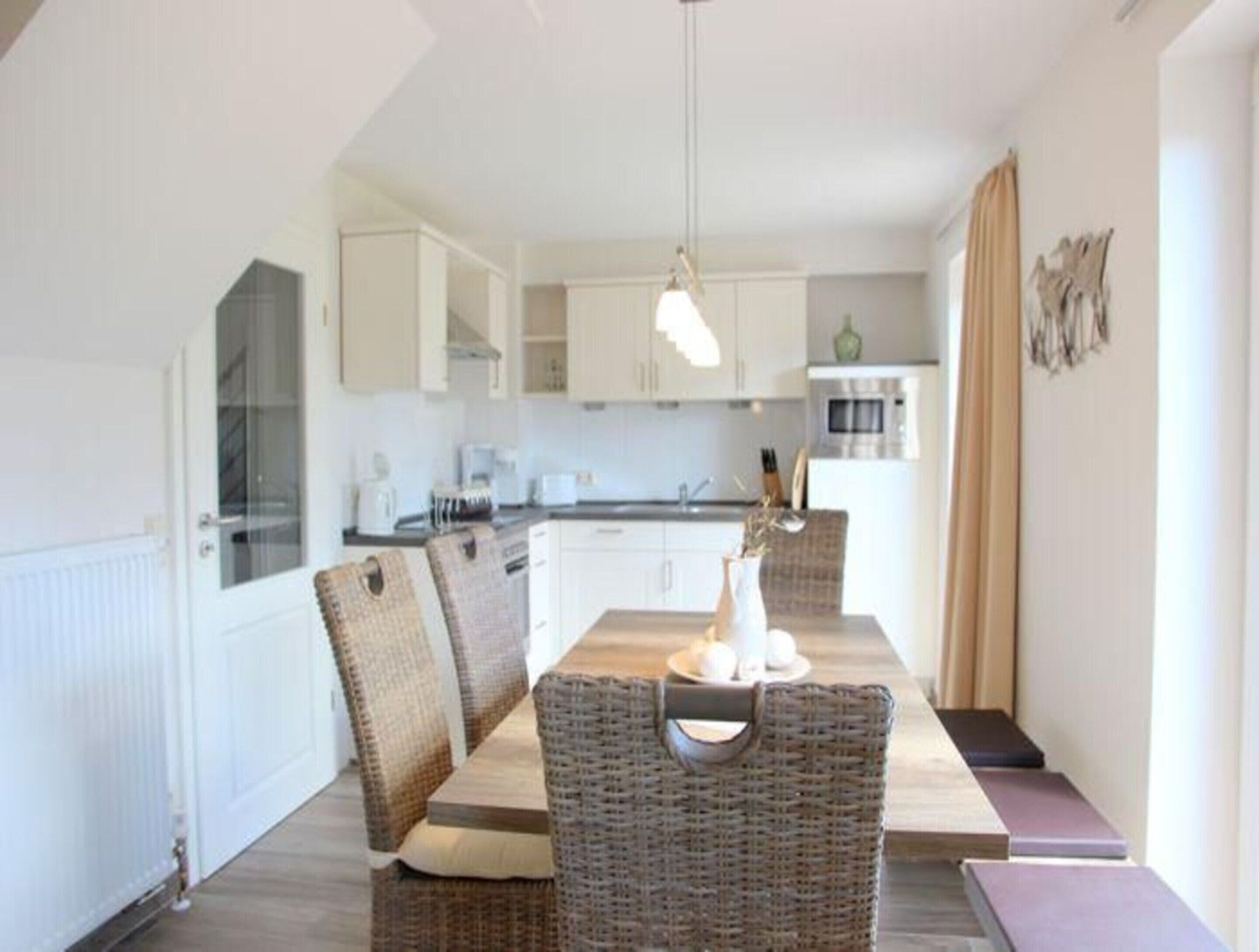 A modern kitchen with white cabinets, a dining table with wicker chairs, and a pendant light.