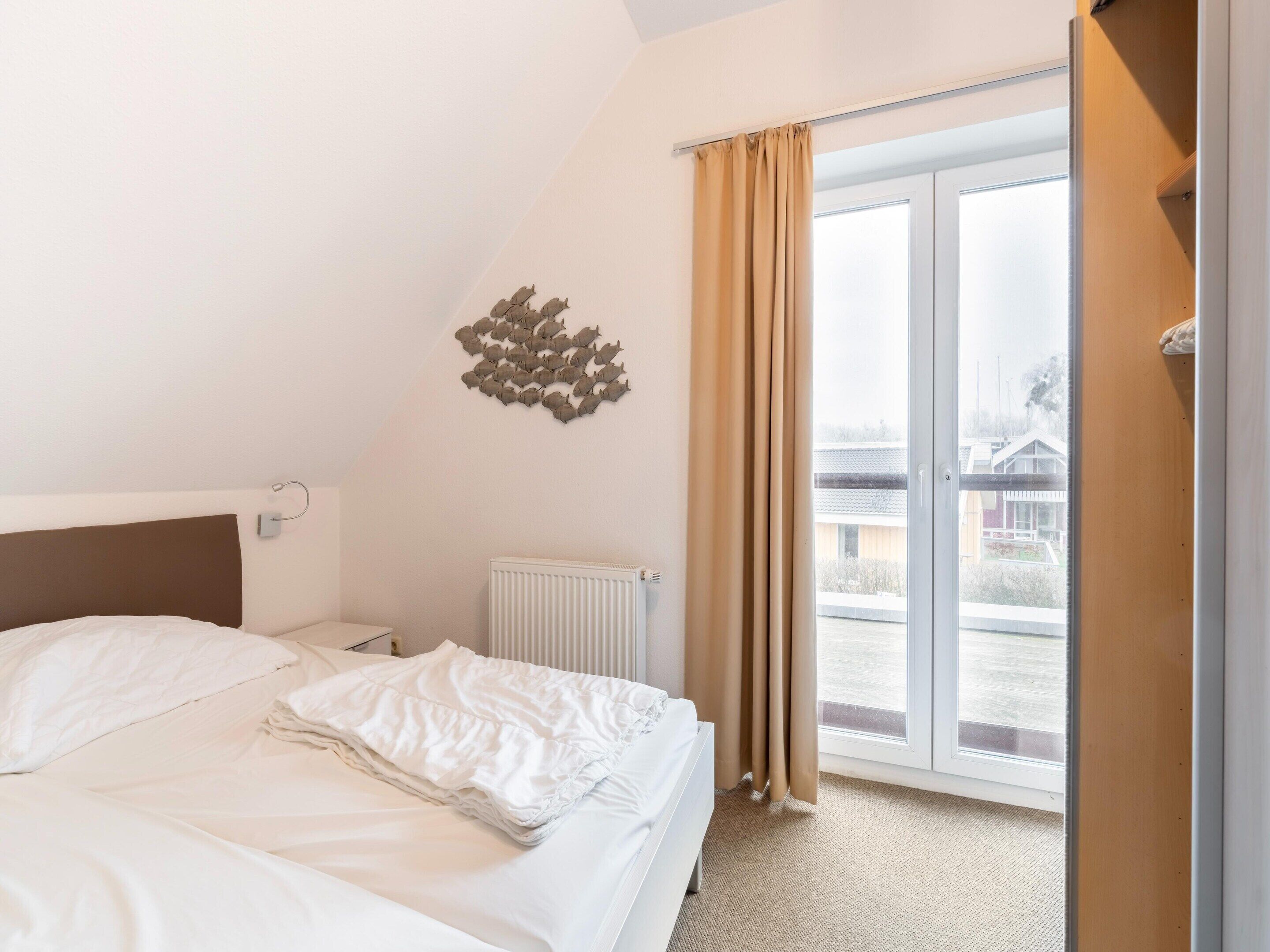 A hotel room with a bed, a radiator, a window with curtains, and a wall decoration.