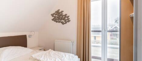 A hotel room with a bed, a radiator, a window with curtains, and a wall decoration.