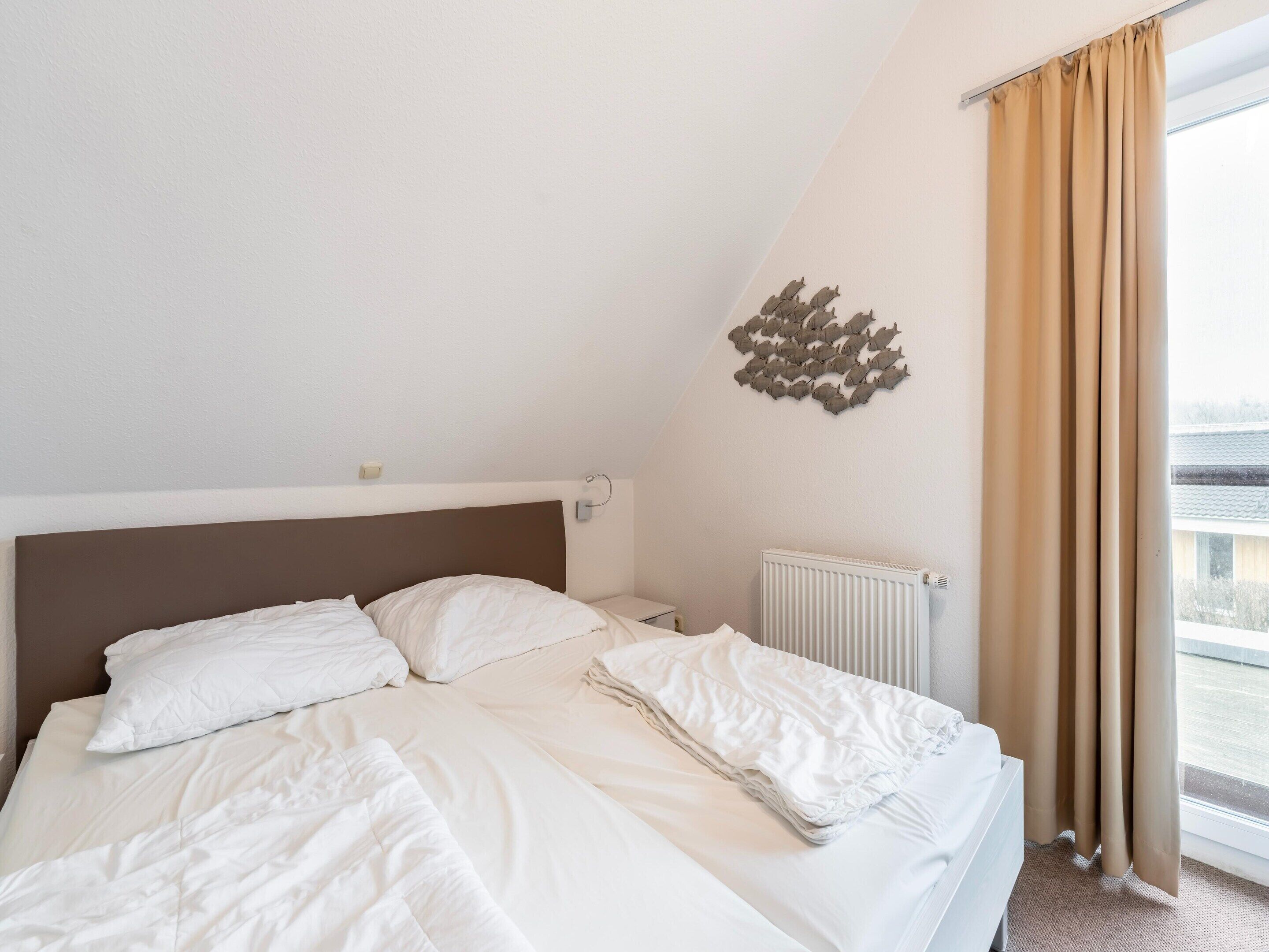A hotel room with a bed, a radiator, a wall-mounted light, and a view of the outside.