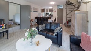 A modern living room with a sofa, a coffee table, and a vase of flowers. There is a staircase with a wooden finish and a modern kitchen in the background. - Spacious Holiday Home With Sauna Near Beach (Wemeldinge)