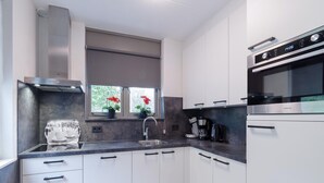 A modern kitchen with white cabinets, a stainless steel range hood, a built-in oven, and a window with red flowers. - Spacious Holiday Home With Sauna Near Beach (Wemeldinge)