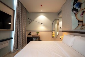 A hotel room with a bed, a desk with a chair, a television, a mirror, and a window with curtains. - SeSaya Poshtel & Bistro - Colombo's Newest and Finest Poshtel Dorms and Rooms (Sri Jayawardenepura Kotte)