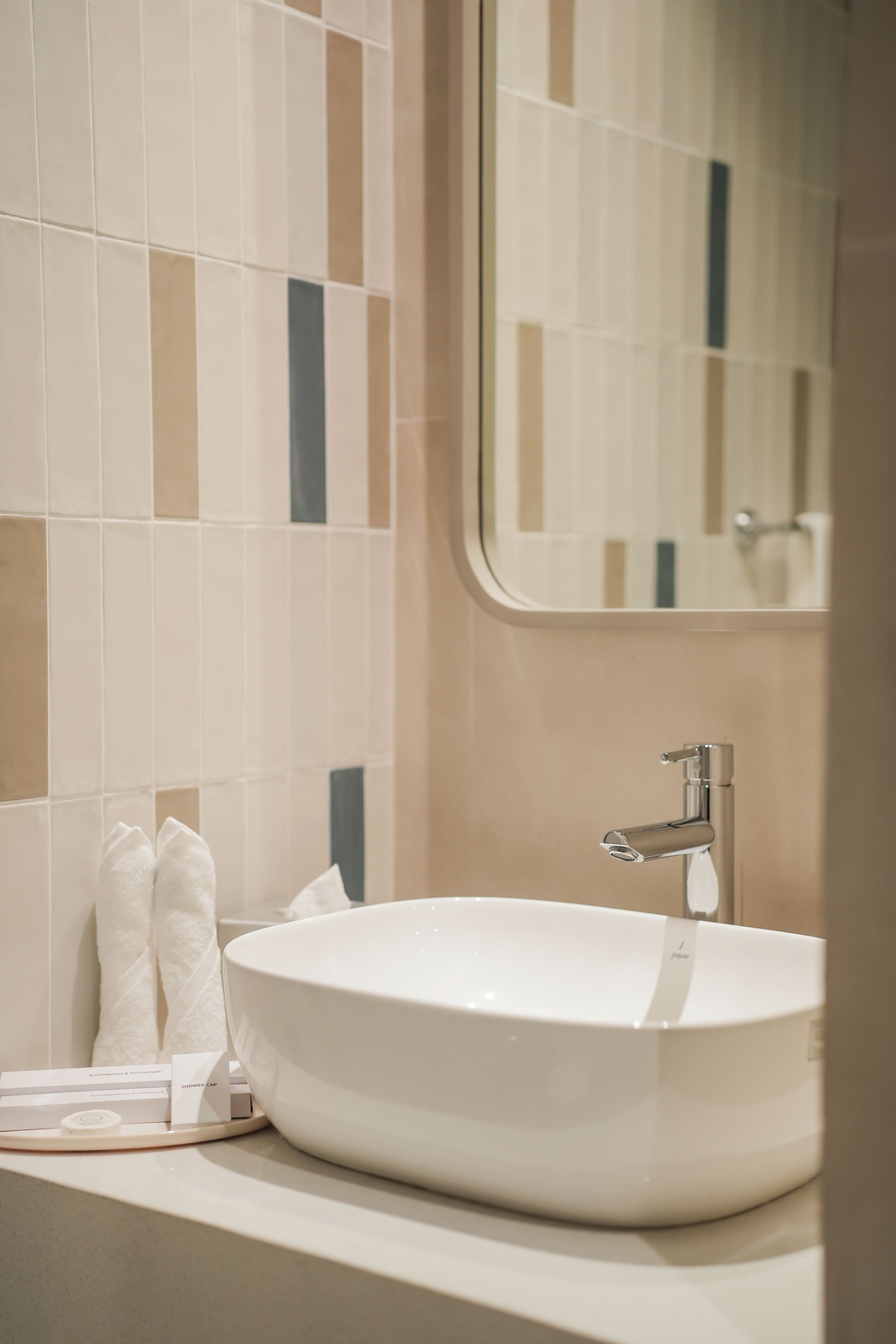 A bathroom with a large white sink, a mirror, and a tiled wall.